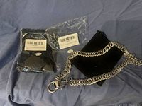 Silver wallet chain, black pouch, and sealed plastic packaging laid on a blue fabric surface.