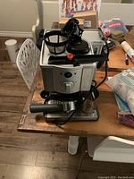 Front view of assembled machine on wooden table with portafilter and milk pitcher