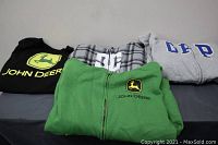 Photo of all four sweaters laid out - black John Deere sweatshirt, green John Deere zip-up sweater, plaid zip-up sweater, gray Gap hoodie