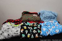 Photo of multiple children's onesies and pajamas folded and laid out showing the various colorful patterns and styles included in the lot.