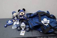 Photo showing the full lot contents arranged on a table including Toronto Maple Leafs duffle bag, plush toys, souvenir cups, hockey puck, goalie mask, and pins.