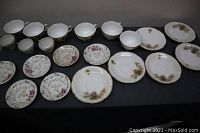 Full view of the tea cups and saucers arranged on a dark surface showing the quantity and variety in the set.