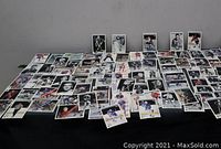Wide shot showing a large selection of loose hockey cards spread across a black surface, varying in size and style, mainly vintage hockey cards.