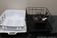 Photo showing a white plastic dish drying rack with plate slotted holder and a black metal wire dish drying rack containing a utensil holder with assorted forks and spoons.