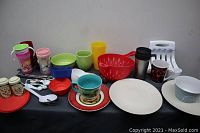 Overview of lot: assorted kitchen cups, bowls, plates, mugs, measuring tools, and spice containers arranged on a table