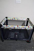 Front view of the fold-up playpen showing mesh sides, colorful top rail, and base with printed instructions