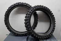 Photo of two Dunlop motorcycle tires standing next to each other showing tread pattern and difference in size.