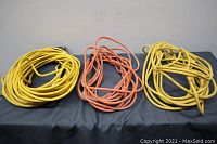 Three extension cords laid out on black fabric, two yellow and one orange.