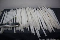 Photo of approximately 70 white twisted plastic ground stakes arranged horizontally on a black surface.