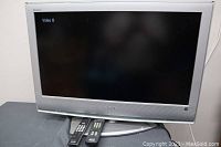 Front view of the Sony Bravia 37-inch TV powered on, showing two remotes on the stand below the screen.