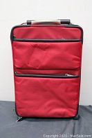 Front view of red fabric suitcase showing two zippered pockets and telescoping handle.