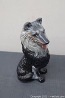 Front and side view of ceramic collie dog figurine showing detailed face, fur texture, and sitting posture on a dark surface.