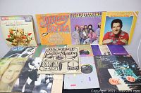 Wide view showing nine vinyl record albums laid out, various artists and album art, covers showing visible wear.