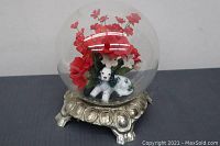 Snow globe style art piece with dog figurine and red flowers on ornate silver-tone base, front angle.