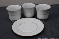 Three white fine china tea cups with silver rims and ribbed lower areas paired with one saucer in front, showing minor wear and slight discoloration around edges.