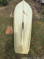 Full underside view of canoe showing length and color with paddles and oars beside it