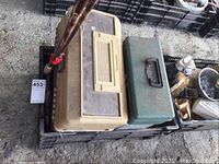 View of plastic and metal toolboxes with two long handles resting beside them in a plastic crate.
