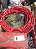 Coiled red air hose, yellow ratchet strap, and two metal anchor hooks in a box
