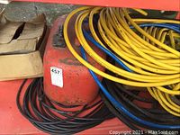 Photo of red gasoline tank with coiled yellow, blue, and black hoses around it.