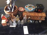 Full view of all items including tins, bottles, spice rack, mortar and pestle and basket with utensils on black surface