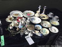 Wide view of all decorative plates, coffee cups, salt and pepper shakers, and other assorted items on a black surface.