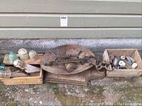 Wide view of vintage metal balance scale and two wooden crates with glass insulators and electrical insulator components arranged outside against building wall.