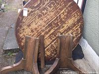 Photo of the round wooden table top leaning against a wall alongside two wooden folded bases