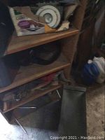 Wooden shelving unit with various items including a box of Glidden paint supplies and a white ceiling light fixture, metal filing drawer leaning on itself near the unit.