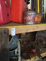 Shelf with red gasoline containers, large red tank, and gasoline cans with visible rust