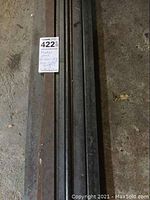 Top view of several long flat and square metal bars with auction inventory tag visible.