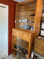 Full view of the wooden cabinet showing the two sections with glass sliding doors, the drawer in the middle, and some decorative items inside.