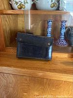 Closed leather carrying case shown on wooden surface with decorative items in background