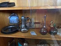 Shelf with silver plated teapot, cream and sugar set, pewter napkin ring and table sweeper pan, and brass bird figures