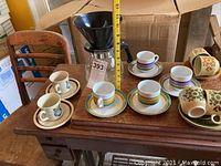 Photo of drip coffee brewer funnel and six coffee cups with saucers on wooden surface showing different floral patterns.