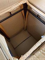 View inside new cardboard box showing metal square frame wrapped in cardboard and packing