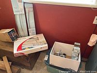 Overall view of the lot showing boxed and loose items against a red wall, including faucets and towel racks.