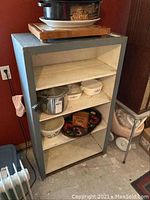 Front view of the wooden shelving unit showing four fixed shelves with some bowls and a tray on top. The shelves and outer frame have visible wear and paint chipping.