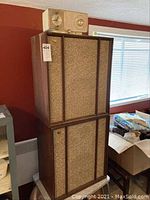 Pair of tall vintage Warfedale speakers with wood veneer and fabric grilles stacked one on top of the other, with a vintage GE clock radio placed on top.