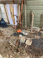 Overview of lot showing tools with handles arranged near wall with various tool heads on ground including shovels and axes.