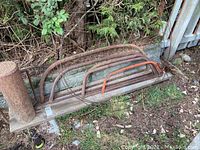 Three rusty bow saws and coiled metal chimney brush laid on a wooden plank outside by foliage.