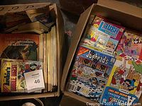 Two cardboard boxes filled with stacks of vintage comic books showing assorted Archie series digests and other titles