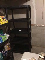 Photo of one black plastic shelving unit with five tiers, showing sturdy construction and open grid shelves in a basement setting.