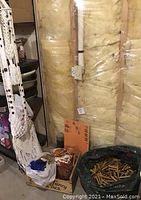 Three off-white macramé plant hangers hanging against insulated wall, some with dark wood beads, showing detailed knotting and fringe tassels