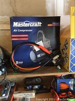 Mastercraft air compressor in box with attached hose and visible accessories on shelf
