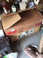 Two large stacked cardboard boxes under shelving with birdhouses visible above