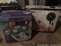 Photo of boxed Conair Whirlpool Massaging Foot Spa and Comfortmate fan boxes on floor.