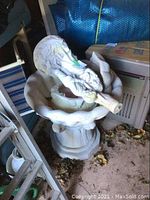 Side view of the entire fountain showing the statue of lady and man under umbrella lying on its side with basin base.