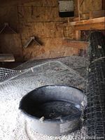 Wide view showing the rolled black wire mesh, round feeding/water bowl, and bedding material covering the floor.