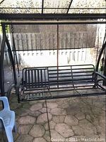 Front view of black metal three-seat swing under canopy