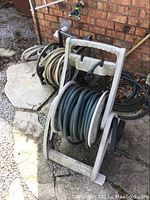 Photo showing two hose reels side by side on a stone-paved ground with attached garden hoses.